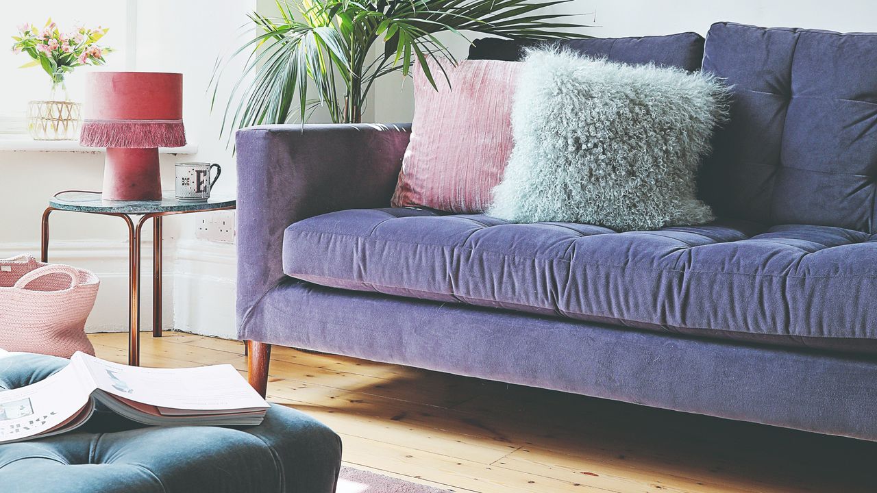 A bright living room with a purple sofa and pink accessories set against white walls