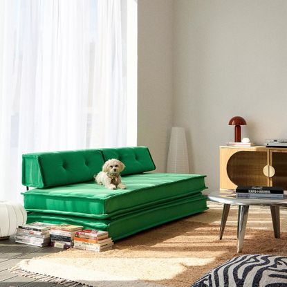 A living room with a green Urban Outfitters sofa bed, a paper floor lamp in the corner and a red mushroom table lamp on a sideboard