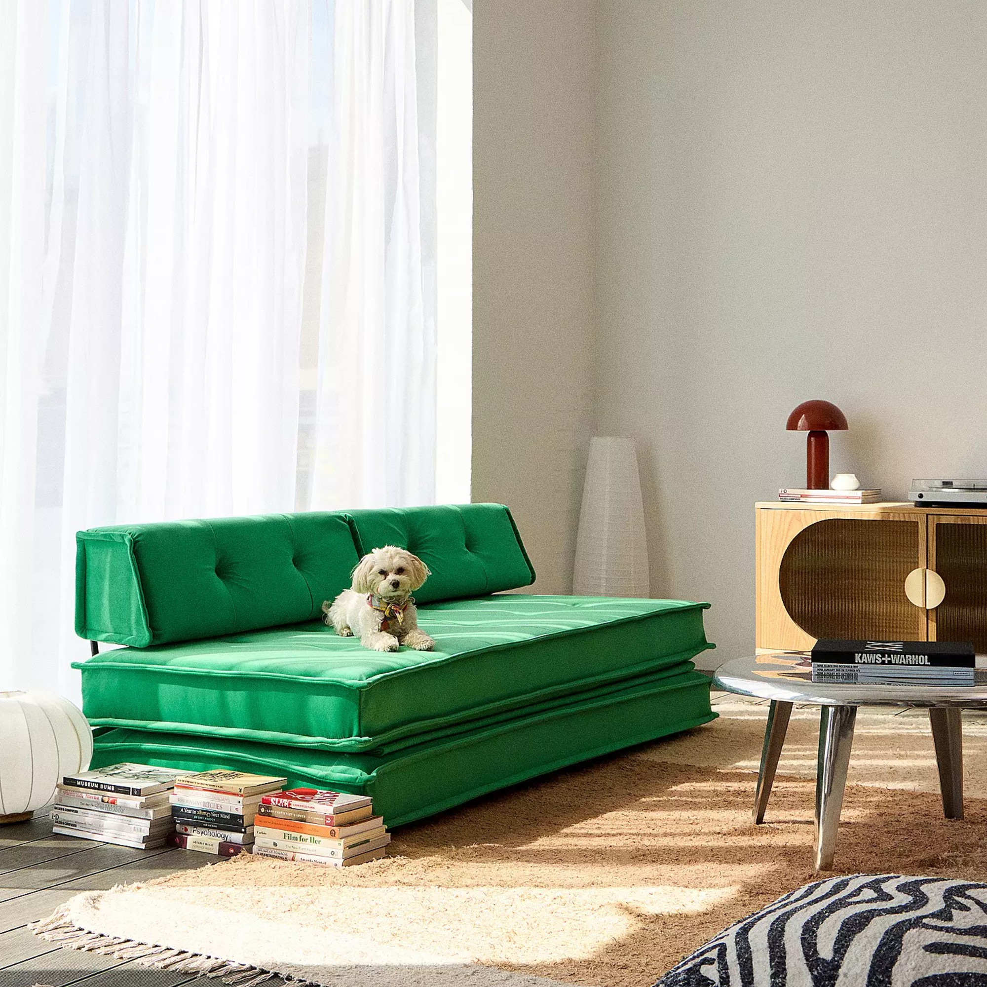 A living room with a green Urban Outfitters sofa bed, a paper floor lamp in the corner and a red mushroom table lamp on a sideboard