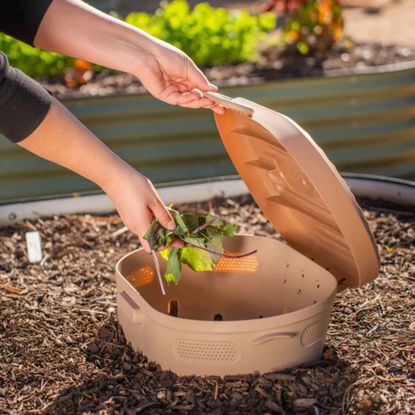 Woman places food scraps in plastic bin in garden