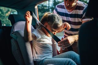 Father helping daughter with the seatbelt as she sits in her car seat