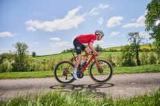 A rider in a red jersey from side-on with fields and blue sky in the background