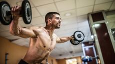 Man performing dumbbell lateral raises during upper body workout using two dumbbells