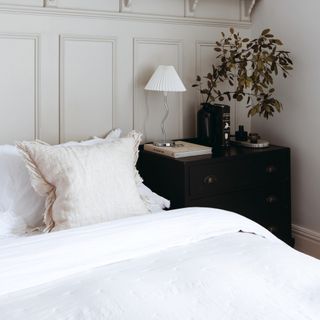 Panelled bedroom wall, bed with white bedding, black bedside dresser