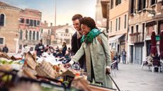 A tourist couple in Venice pause to look at the offerings at a street market.