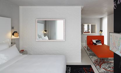 Bedroom in the Mama Shelter hotel, Istanbul with white walls and bedding, large mirrors and a red sofa/bed