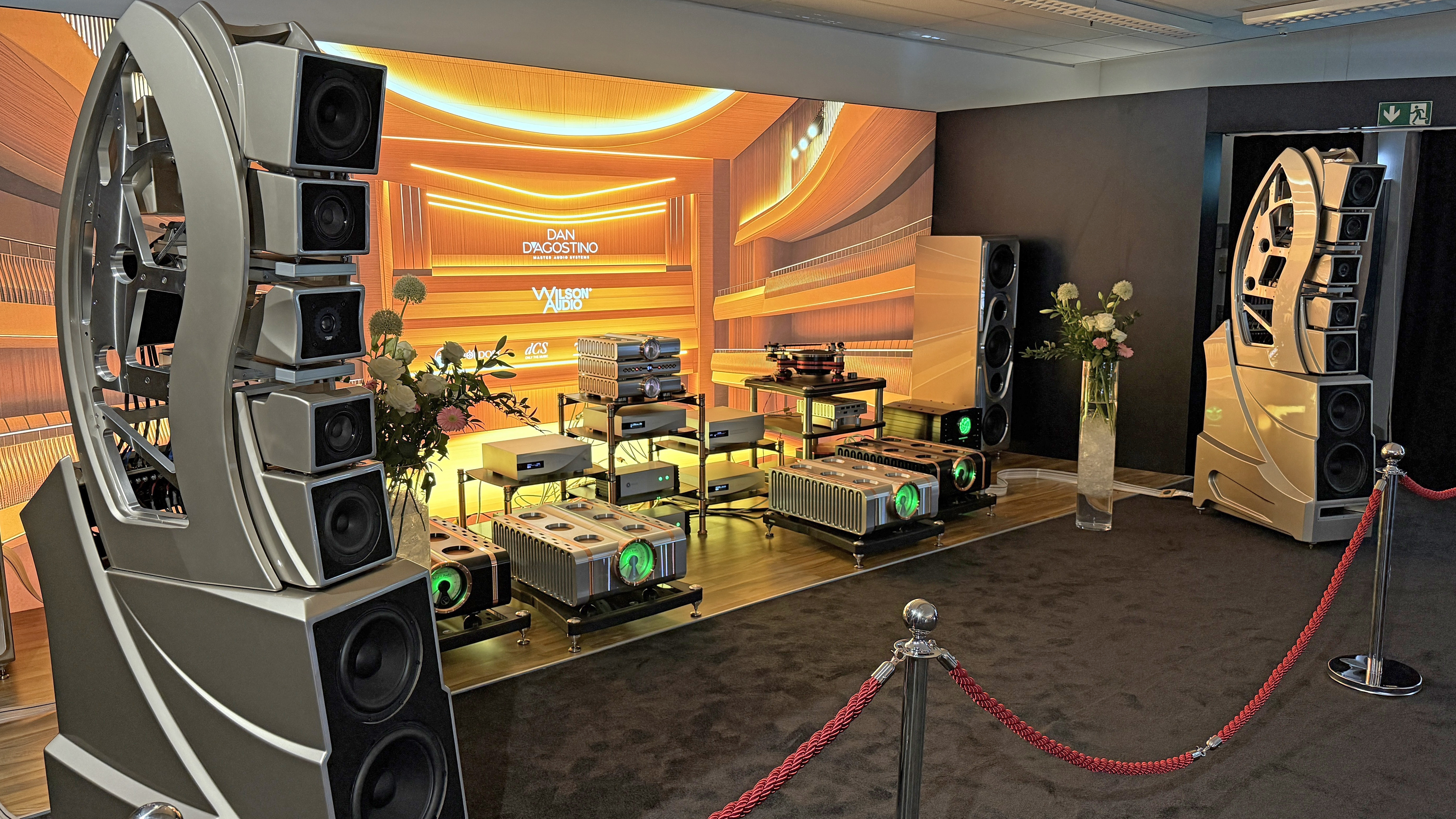 Two huge speakers flank a huge number of amplifiers and other hi-equipment, on a stage, behind a velvet rope