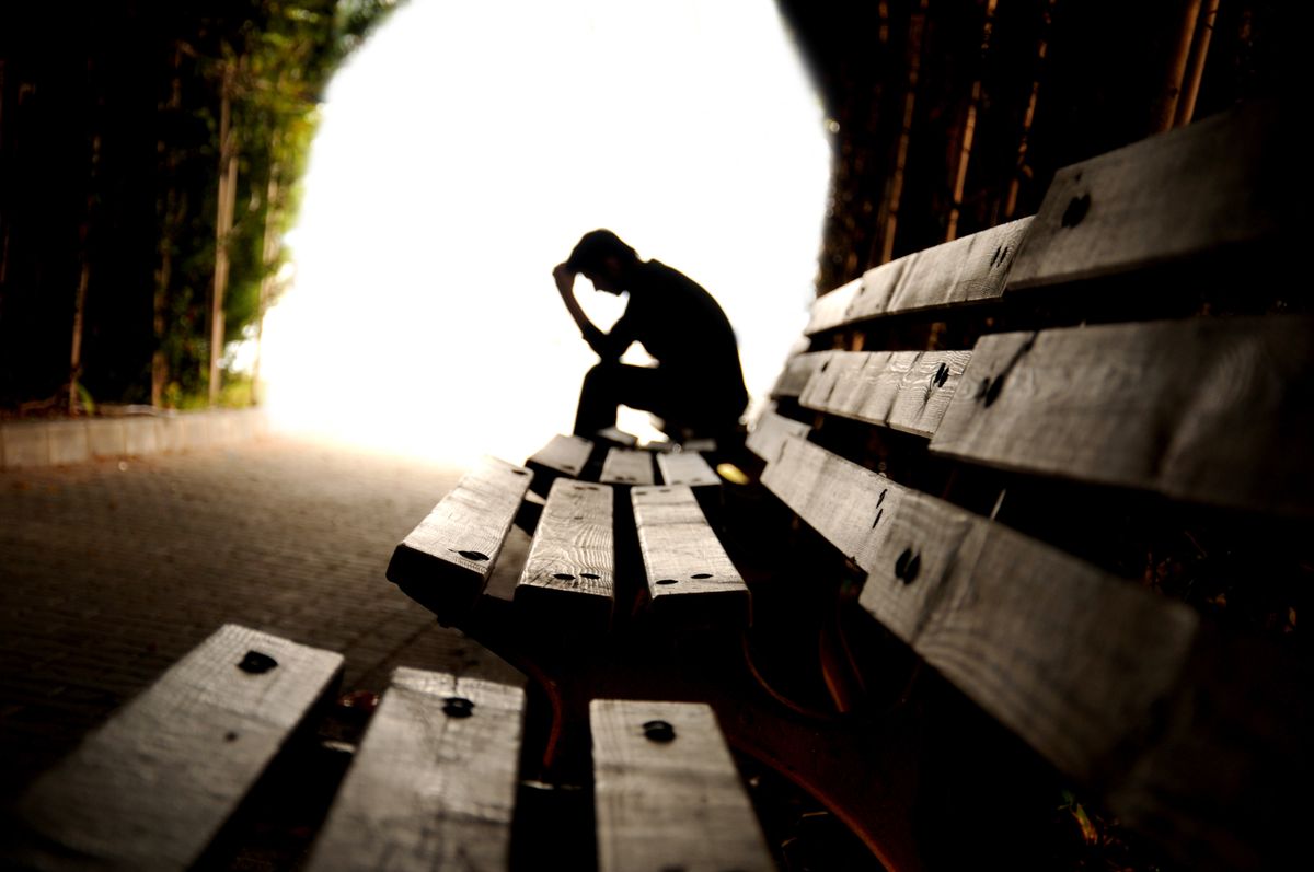 Person sitting on a bench with hand on forehead.