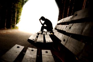 Person sitting on a bench with hand on forehead.