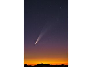 a photograph of a large comet at sunset with the silhouette of mountains visible