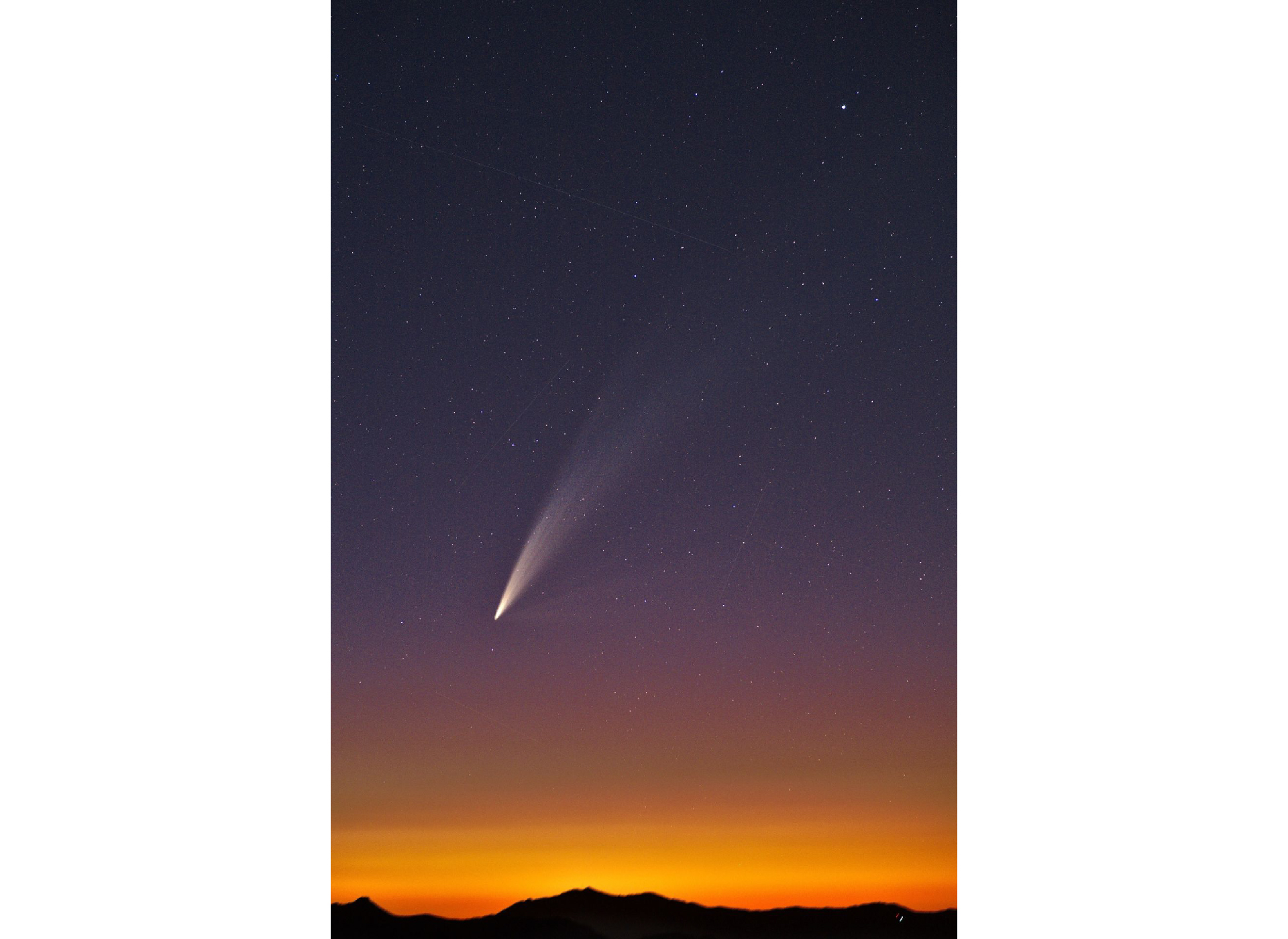 a photograph of a large comet at sunset with the silhouette of mountains visible