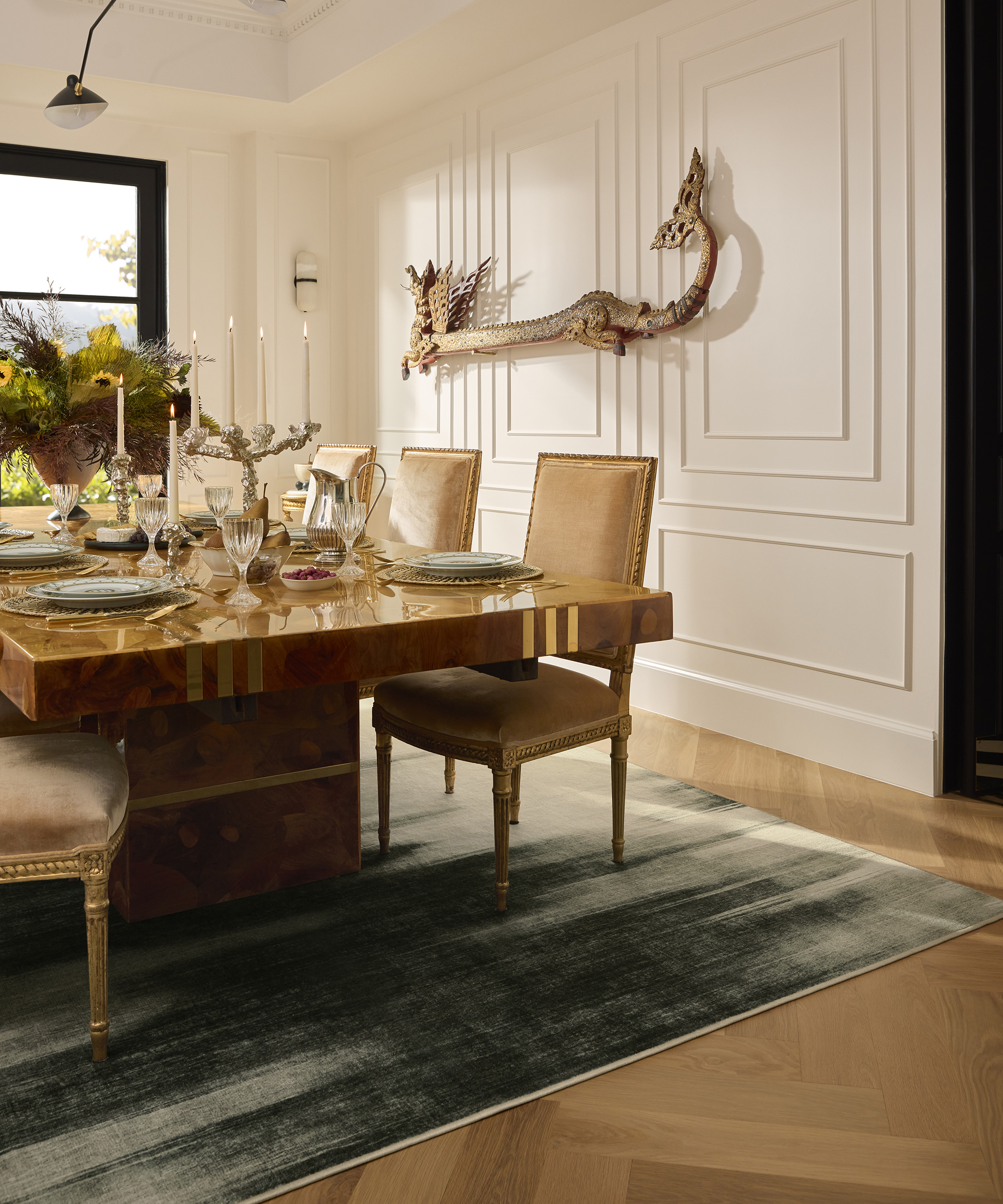 large dining room with gray rug under a burl wood table and white wood panelling on the wall