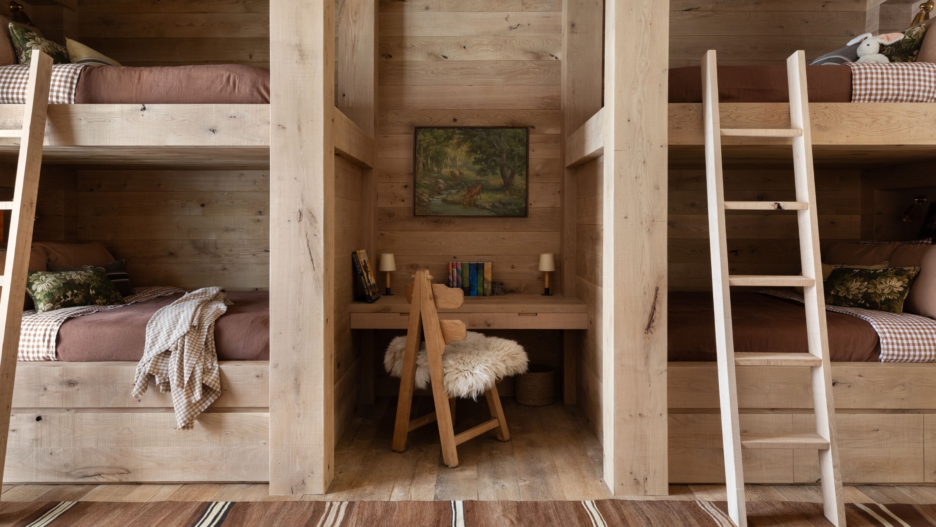 a white oak wood clad bunk room with 4 bunks dressed for kids with a small desk in the middle