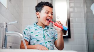 A boy in blue pyjamas cleaning his teeth with an electric toothbrush