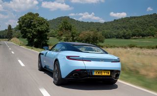 Country road with light blue Aston Martin DB11 driving away