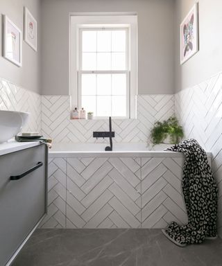 Small white bathroom with herringbone layout of white metro tiles on wall and bath side