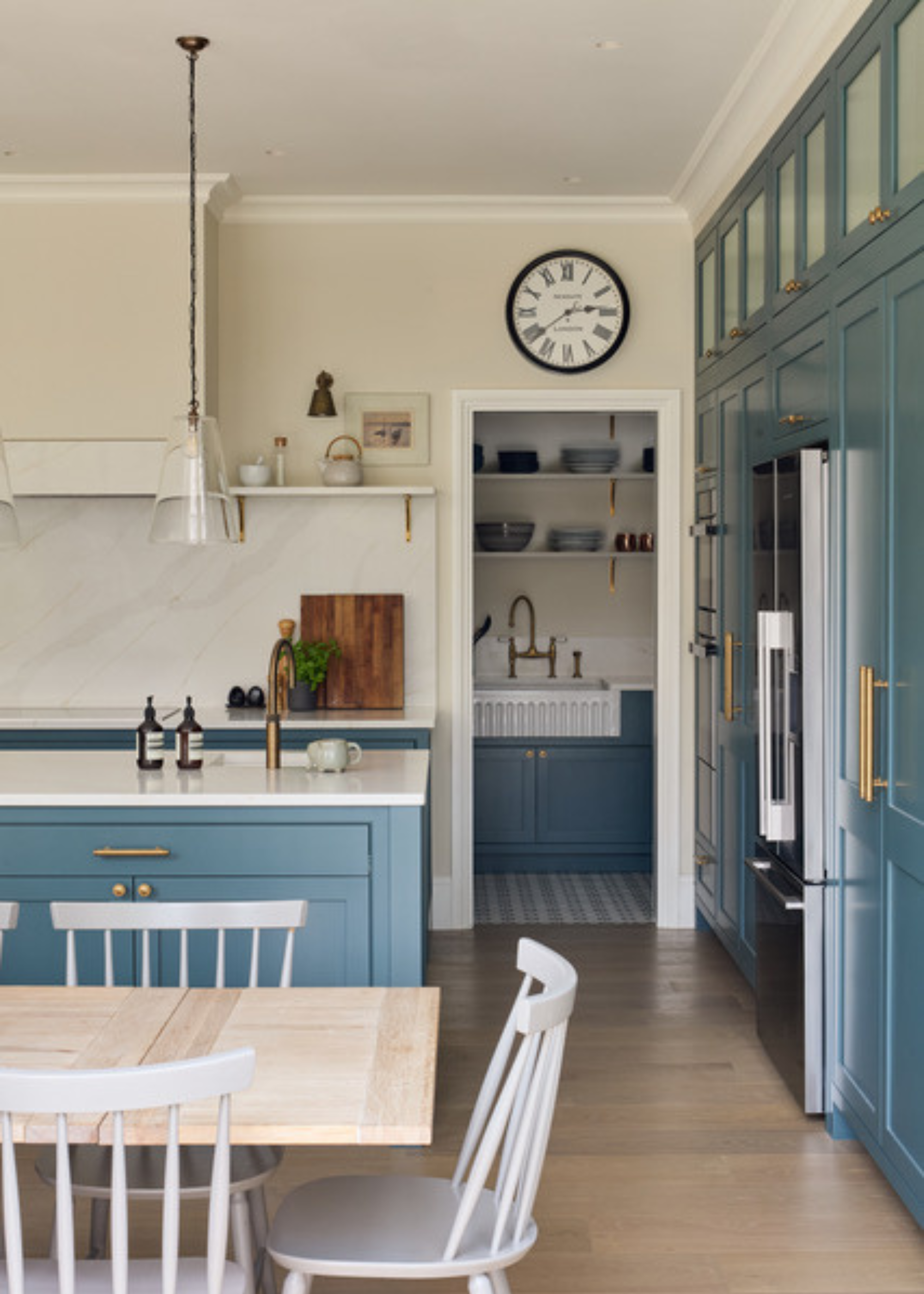 A mid tone blue kitchen diner with brass hardware and a peep through to the scullery