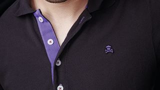 Close up of an unbuttoned polo shirt with Johnny Cupcakes logo embroidered on right