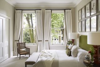 white/cream bedroom with green headboard, cream wallpapered walls, artwork, double windows drapes