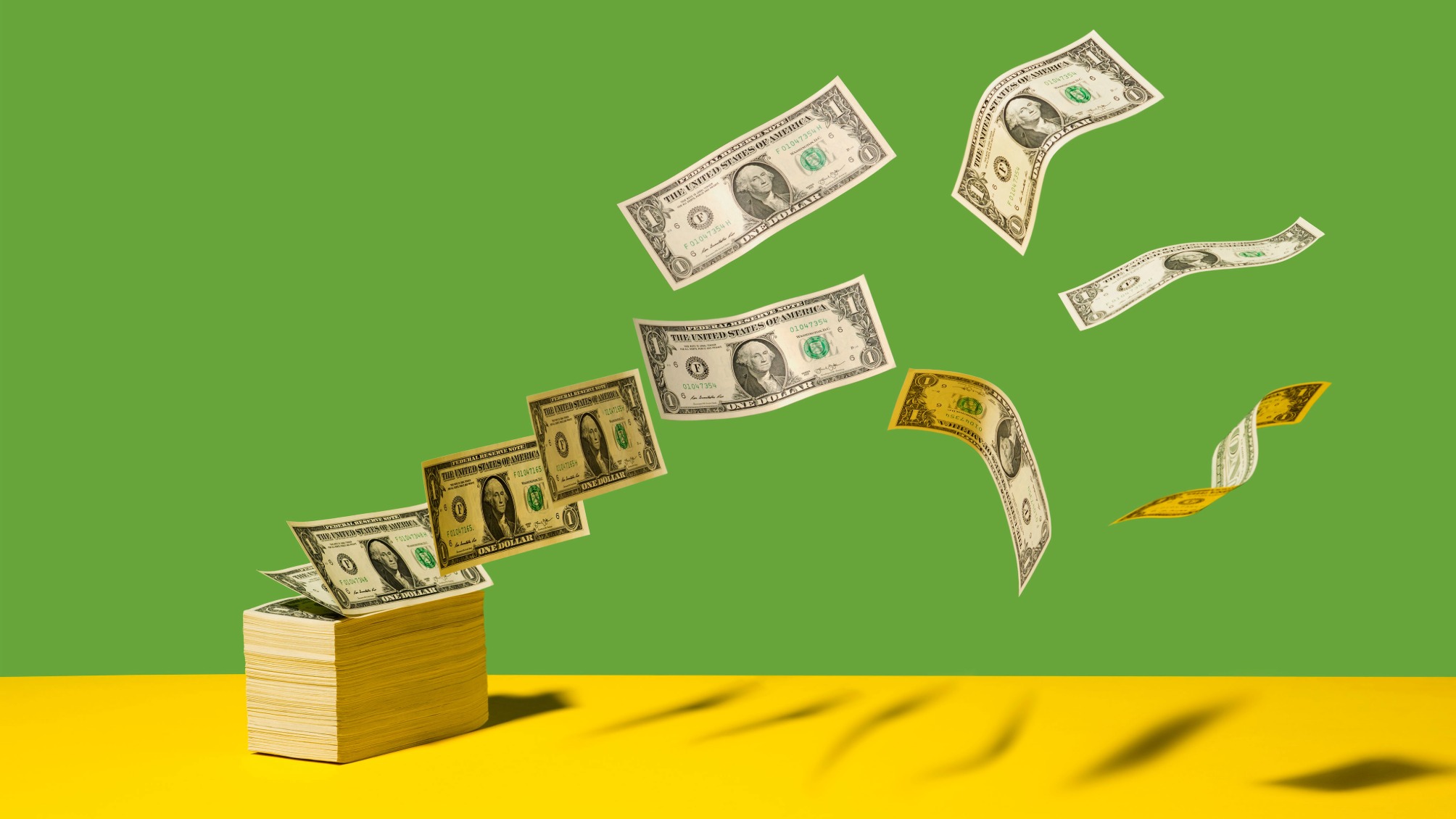 Stack of US $1 bills with bills flying away on yellow shelf, green background