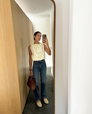 Woman wears a white tank top with Khaite jeans and slippers.