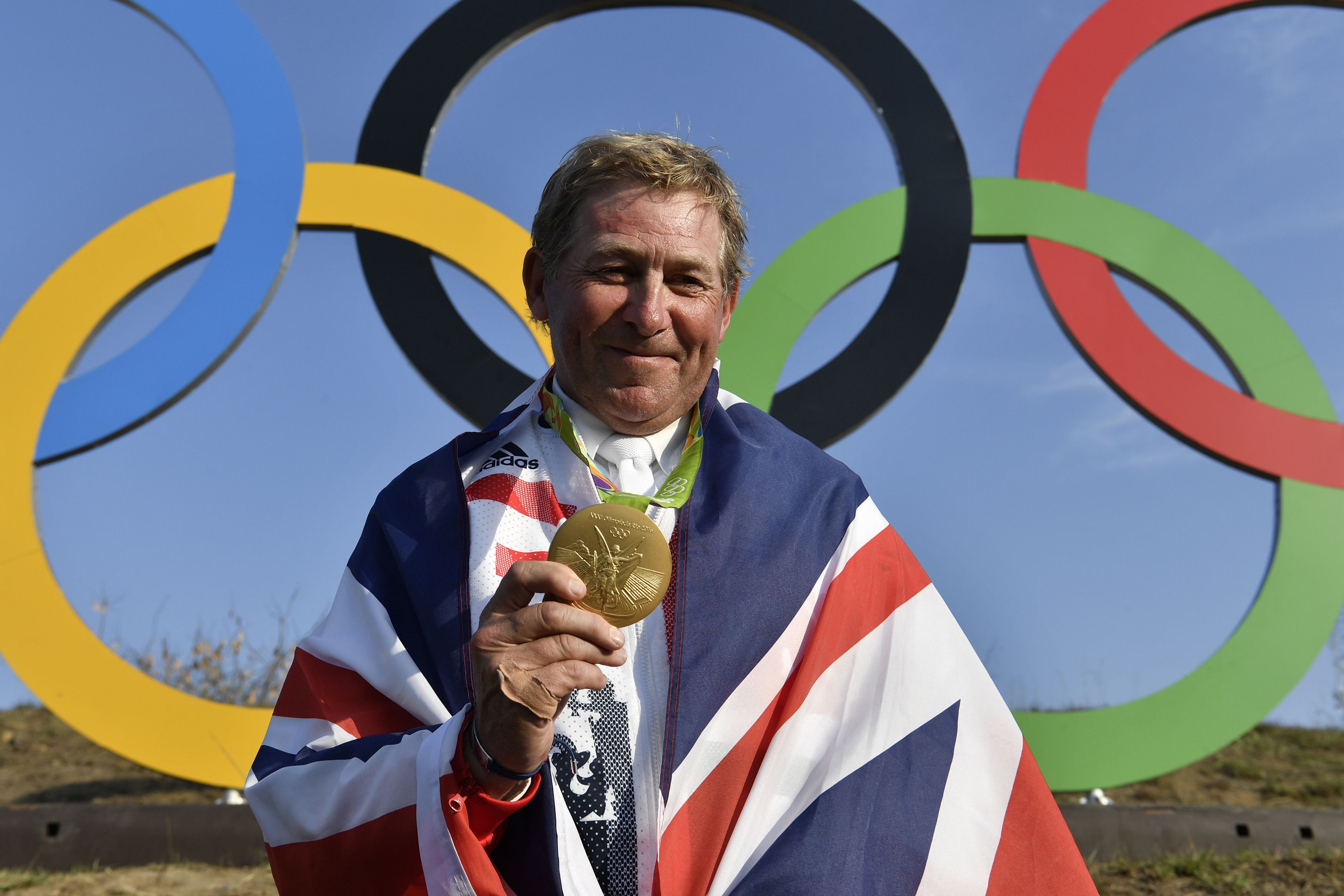 Britain's Nick Skelton celebrates with his gold medal in front of the Olympic rings after the individual equestrian show jumping event during the Rio 2016 Olympic Games in Rio de Janeiro on August 19, 2016. / AFP / John MACDOUGALL (Photo credit should read JOHN MACDOUGALL/AFP/Getty Images)