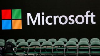 A very large version of the Microsoft logo is written on a wall, with conference chairs arranged in front of it. One of the chairs has a backpack sitting on it.