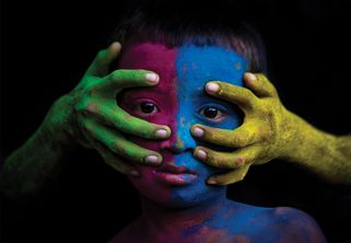 Attach: A boy with a colourful painted face taken during Holi festival. His sad-looking eyes seem to convey a sense of not being able to escape from some unknown worry or sorrows.