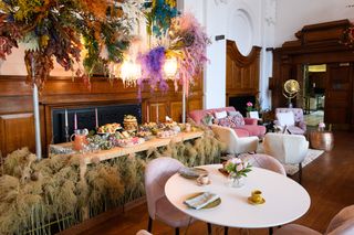 Feather and floral decor in wood paneled room with modern round dining table and pink velour upholstered chairs