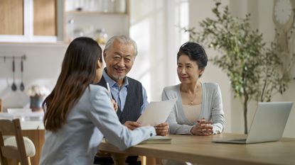 An older couple talk with a financial adviser at their dining room table.