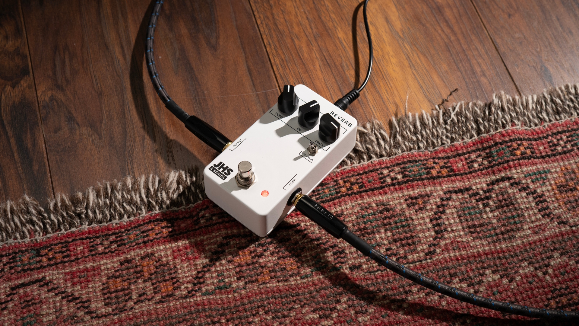 A JHS 3 Series Reverb pedal on a rug with guitar and power cables plugged in