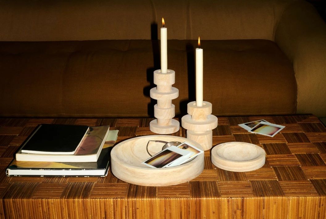A series of stoneware home accessories, including two bowls and two sculptural candle holders, sit on a wooden table.