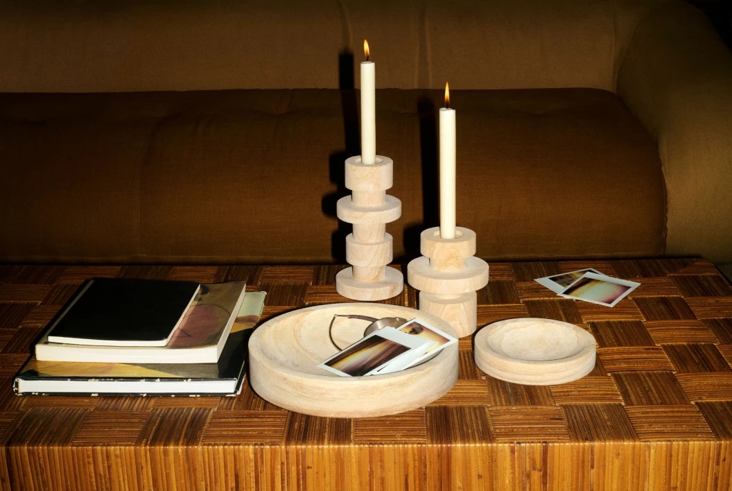 A series of stoneware home accessories, including two bowls and two sculptural candle holders, sit on a wooden table.