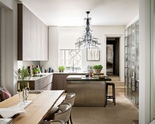 A neutral kitchen with large chandelier and wooden dining table.