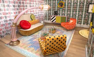Always Close installation by Studio Job in Luxembourg. A colourful room with a hot dog shaped sofa, patterned chairs, a glass coffee table, a patterned console and a street light shaped floor lamp.
