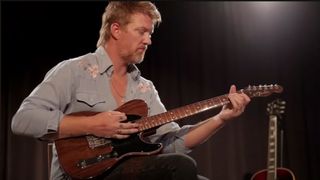 A still from a video of Queens of the Stone Age frontman Josh Homme wearing a blue western shirt and playing George Harrison's rosewood Telecaster.