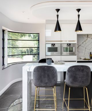 An art deco-inspired kitchen with curved windows, an island and black overhead light fixtures