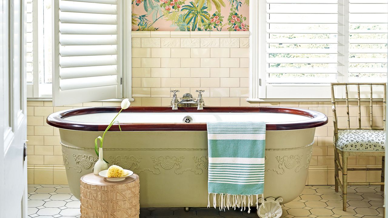 freestanding bathtub against wall with patterned wallpaper and large windows with venetian blinds