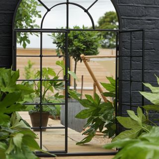large arched garden mirror with plants and foliage, view of the garden through the mirror