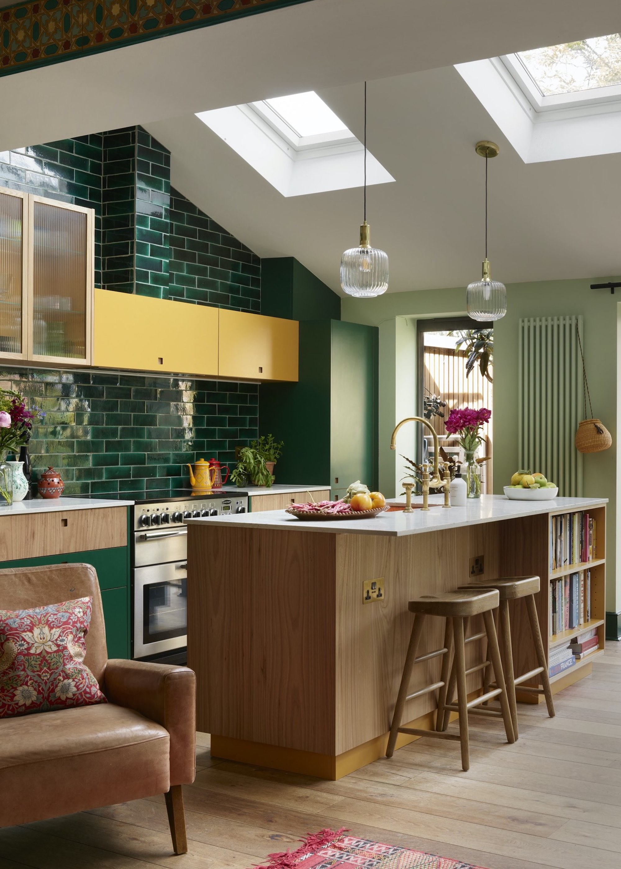 Deep emerald tiles used for the kitchen backsplash in this kitchen extension. Upper cabinets have also been added for extra storage. There is also a large kitchen island with a countertop overhang and bar stools.