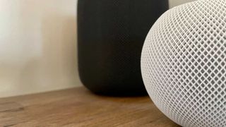 White HomePod mini in front of black HomePod on wooden table
