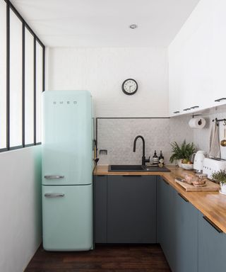 Kitchen area with teal coloured fridge / freezer next to wooden counter top with grey cupboard doors