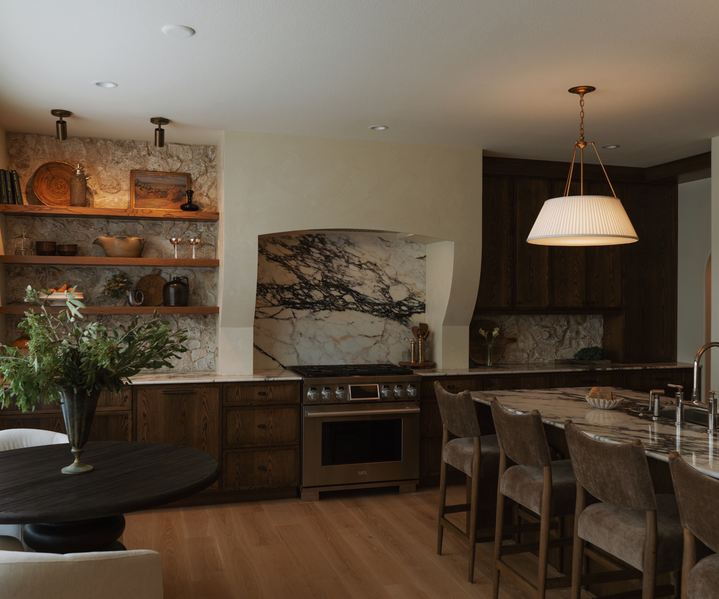 A moody kitchen with wooden cabinets, marble counters and backsplash, and a plastered range hood with a curved profile