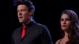 Cory Monteith singing on stage in a suit in Glee.