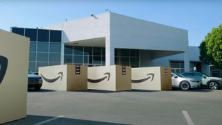 A car parking lot containing cars and giant Amazon boxes