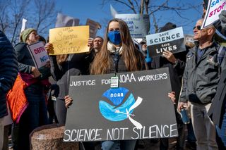 A person at a protest holding a sign that says "justice for NOAA workers" and "science not silence."