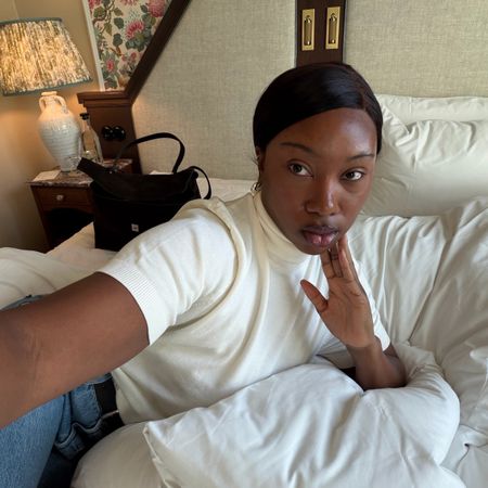 Photo of a woman taking a selfie from bed in a white T-shirt and jeans