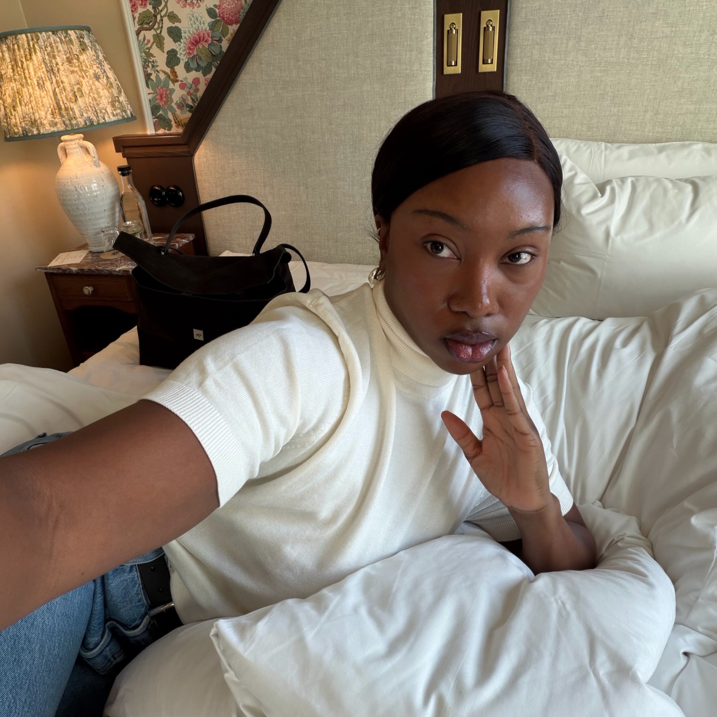 Photo of a woman taking a selfie from bed in a white T-shirt and jeans
