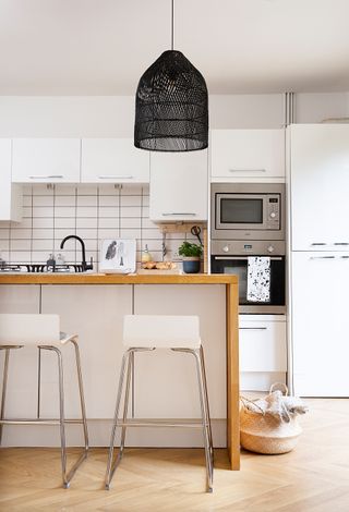 A white kitchen with black pendant light, wood effect flooring, in-built microwave oven and conventional oven