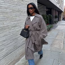 Influencer @nlmarilyn walks down the street in London wearing chisel toe boots with jeans and a grey trench coat.
